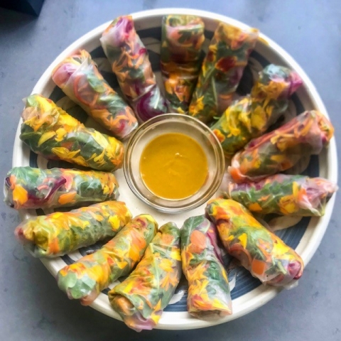 a plate of colorful rice paper rolls surrounding a yellow dipping sauce