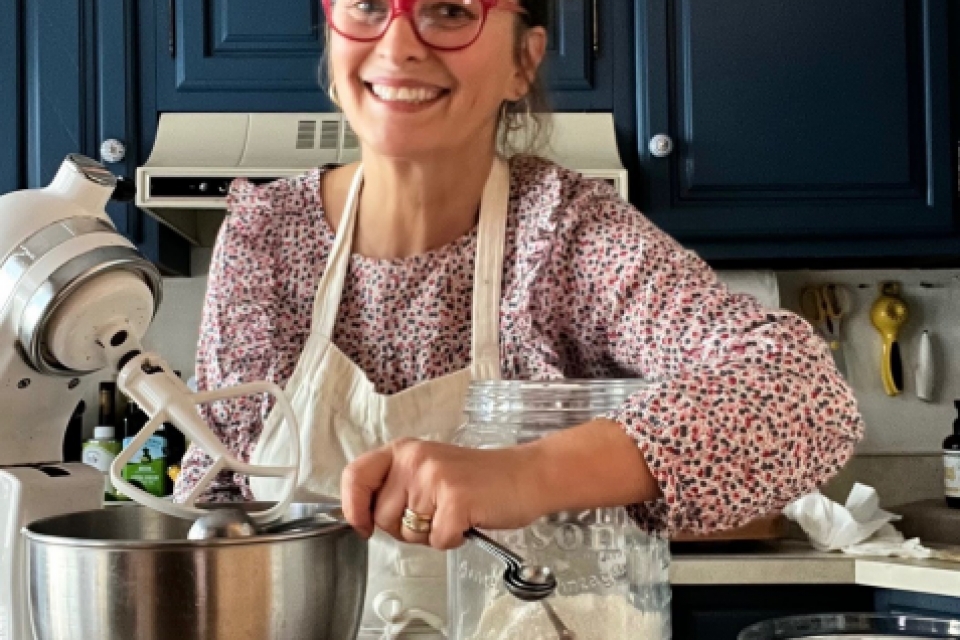 A woman wearing red glasses stands near a mixer and baking ingredients in a kitchen with blue cabinets