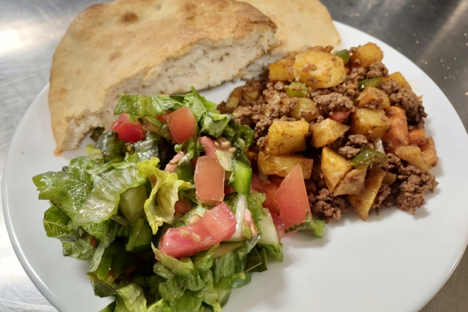 a white plate with a llatbread, salad, and a beef and potato dish