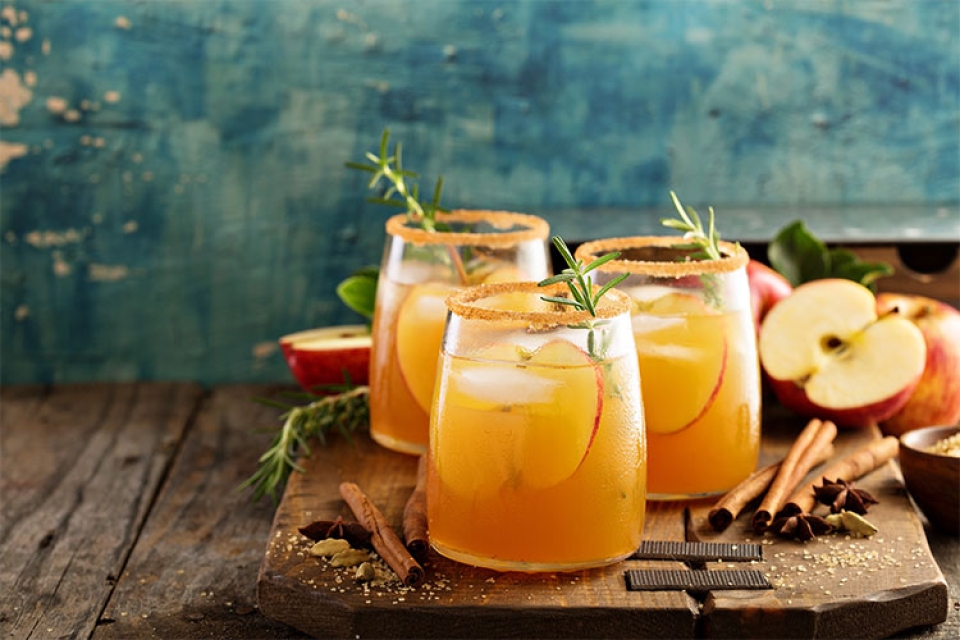 three glasses full of cider and apple slices on a wooden board