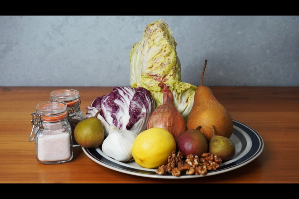 A photo of the ingrediants for the salad. Two different kinds of radicchio, garlic, pears, lemon, garlic and walnuts are arranged on a plate beside jars of salt and pepper.