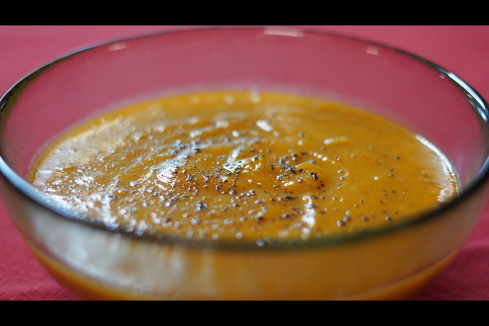 Shot of a clear bowl with an orange soup topped with ground black pepper.