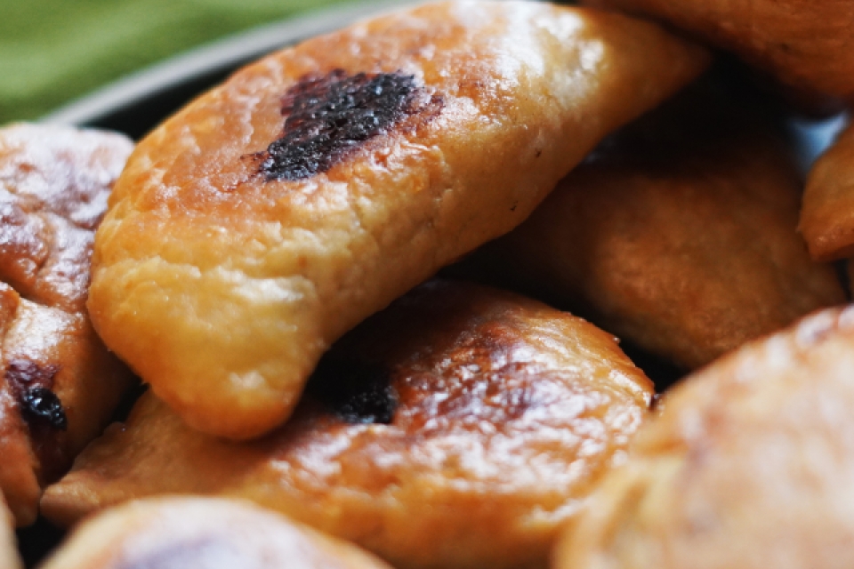 A close up of many turnovers. Many are in soft focus in the foreground of the image, and 2 are in clear focus with bits of browned cheese poking out from the center of the pastry. 