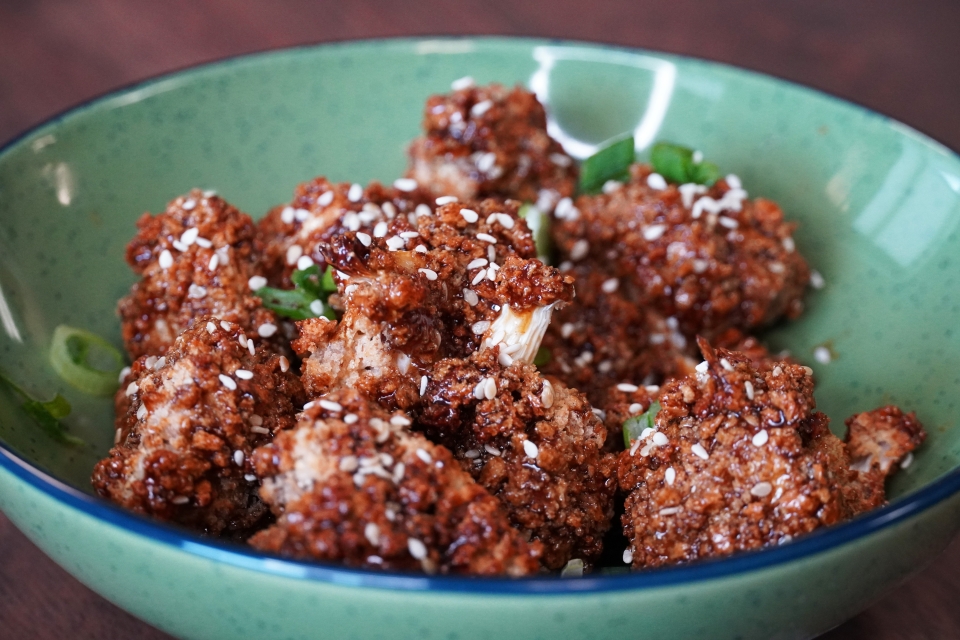 A close up of the fried cauliflower florets in a green bowl. They're a rich brown, and topped with green onions and sesame seeds.