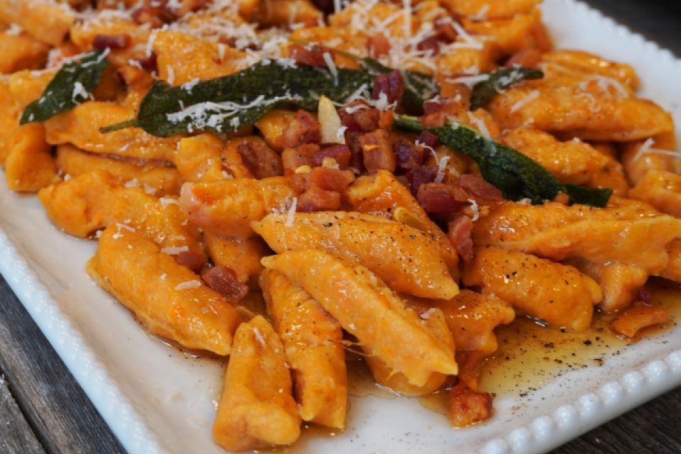 A corner shot of the gnocchi plated on a square white plate. Its topped with fried sage, and parmesean cheese!