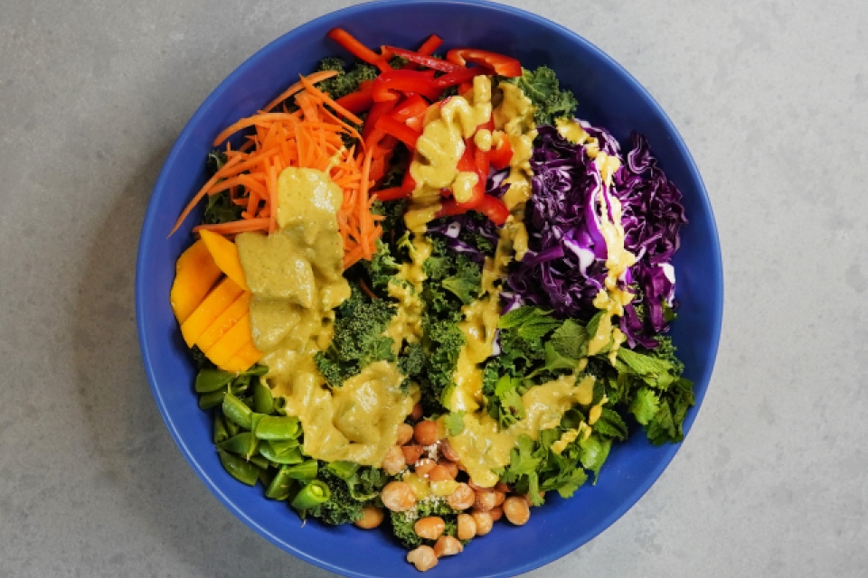 A straight down shot of the bowl of salad. On it you can see the peppers, carrots, cabbage, chickpeas, cilantro, and peas. Dressing is drizzled over all of it. 