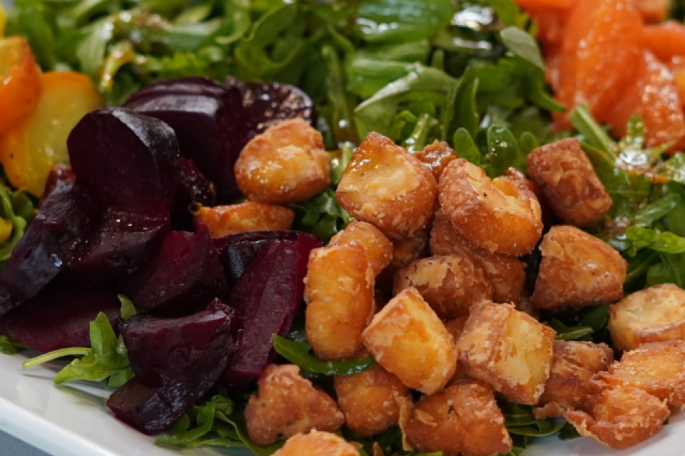 a close up shot of the salad. in the front are the blocks of fried halloumi, beside them are the sliced red beats. Behind them and out of focus are the rest of the salad's toppings.
