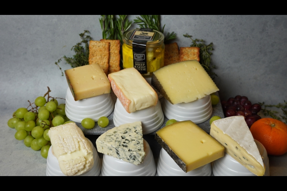 Seven cheeses are arranged on short white pedestals. They are surrounded by laurels made of fruit, herbs and crackers.