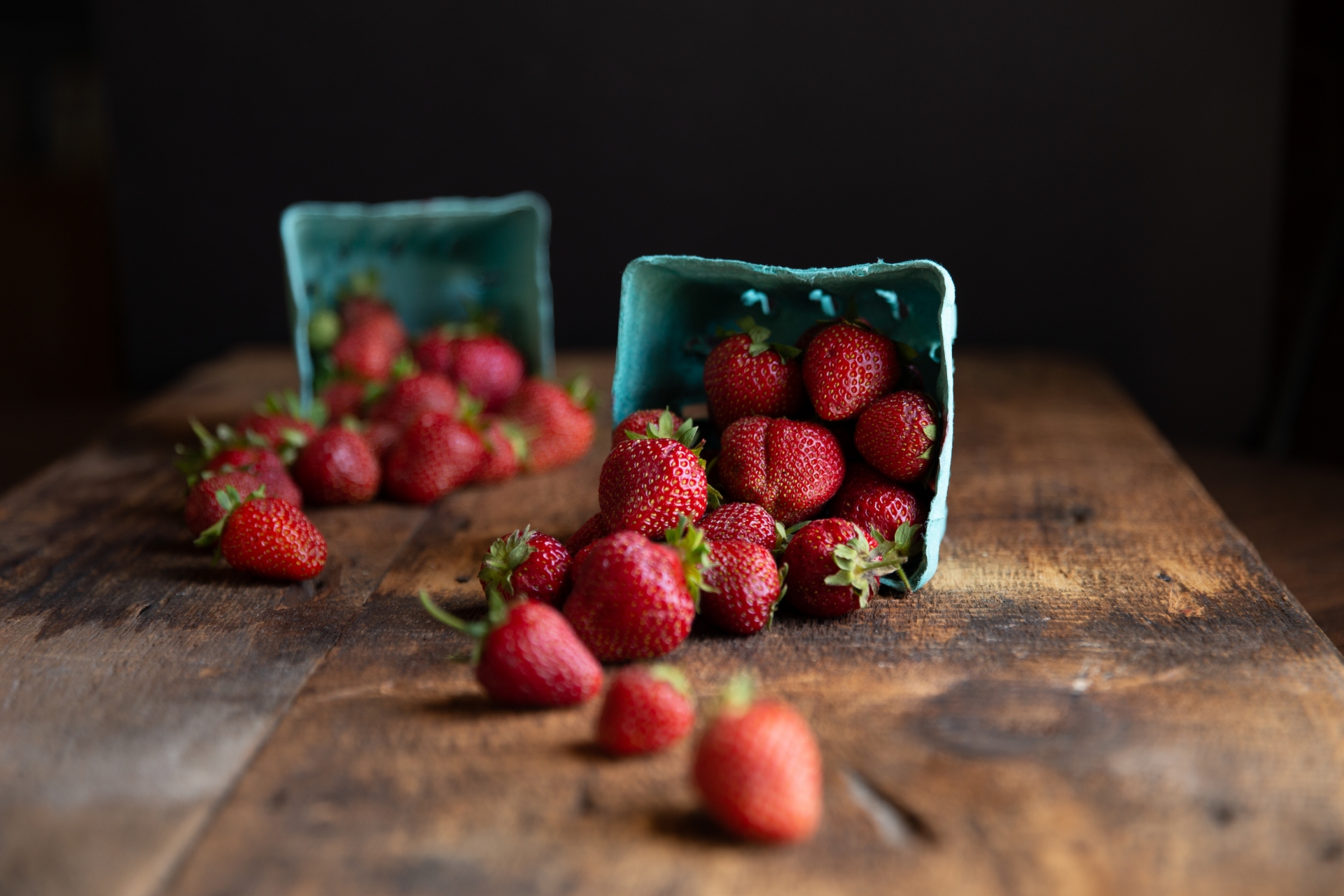 Two pints of strawberries spilled on a wooden table