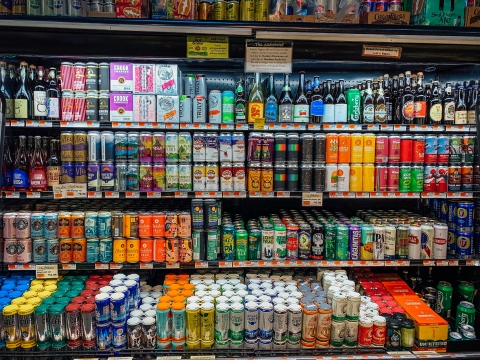 A display case of four shelves, all full with many different, brightly colored bottles and cans of beers and ciders.