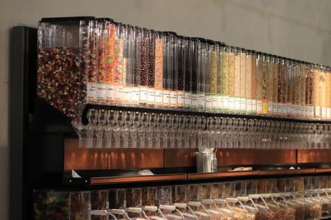 A long row of clear bulk dry goods dispensers. Inside each is a differently colored bulk item, including candies, nuts, beans, grains and more.