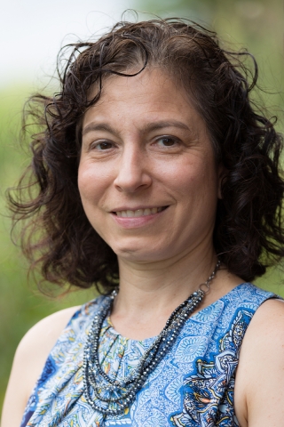 A portrait of Allison Fiore wearing a patterned blue top and blue bead necklace standing outdoors
