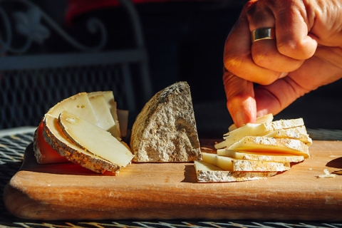 a hand reaching to grab a slice from three piles of sliced cheese on a wooden board