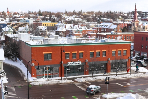 City Market's Downtown location on a wintry day with snow on the ground and the surrounding neighborhood on the hill behind it.