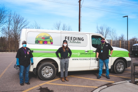3 people are posing outside in front of a white van with a "Feeding Chittenden" logo and green stripe.