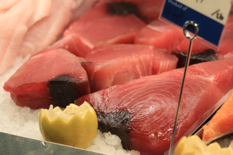 Tuna steaks arrayed on ice. They are very rich pink. In front of the tuna steaks are two half-lemons with the cut side up. 