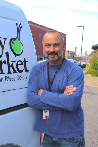 A person in a blue shirt stands next to a van. The van has a City Market logo on the side.