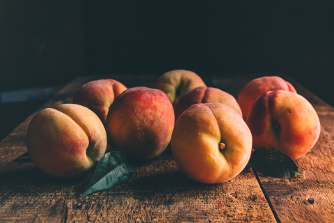 Eight peaches are pictured from the side as they sit on a wooden table.