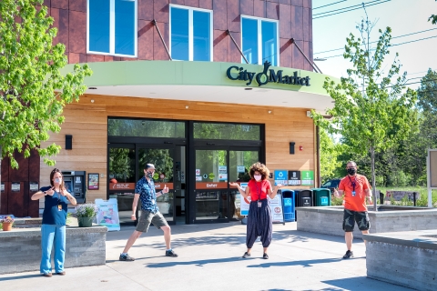 Four City Market employees are standing outside the South End City Market Co-Op on a sunny bright day.