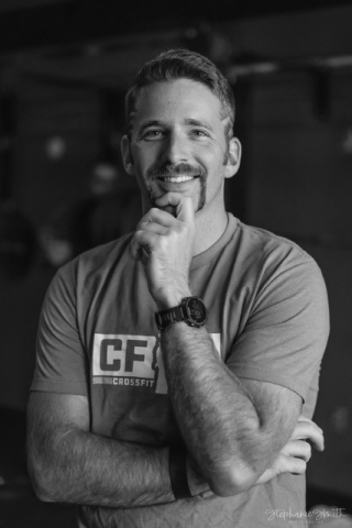 A black and white headshot of Sam Werbel. He has one arm folded over his waist and the other elbow propped on it, with his hand tucked under his chin. He is smiling warmly.