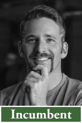 A black and white photo of a person from the shoulders up. The person is wearing a tee shirt and holding their hand up to their chin. Below the photo there is a green box with the word "incumbent" printed in it in white lettering.