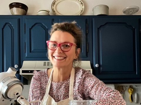 A woman wearing red glasses stands near a mixer and baking ingredients in a kitchen with blue cabinets