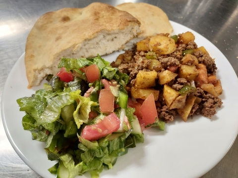 a white plate with a llatbread, salad, and a beef and potato dish