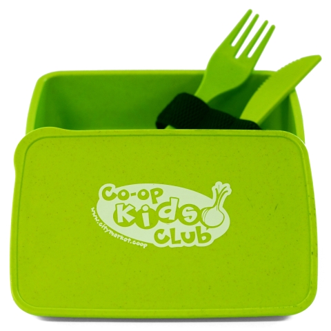A bright green lunch box is open and has its lid propped in front of it. The lid has a Co-op Kids Club logo printed in white in the center. Inside the lunch box are a matching fork and knife, sticking up at a jaunty angle.