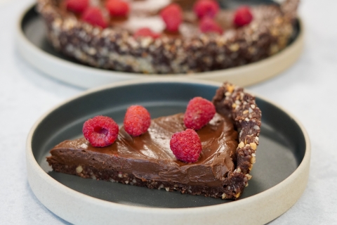 Brown pudding like pie with crust and raspberries topping it on plate with rounded edges. Black interior of plate with slate exterior on white table top.