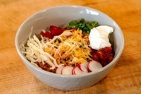 Grey bowl with cheese, sour cream, radishes, cabbage, and chicken on wood background.