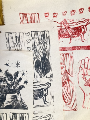 A collection of block prints in blue and red ink on off-white paper. The prints have fine line detail and feature natural figures including plants, leaves, grasshoppers and hands.