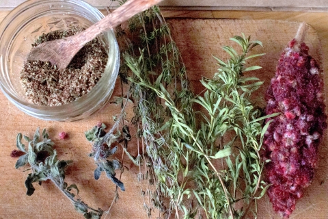 a collection of dried herb stems and a glass jar with a wooden spoon on a cutting board