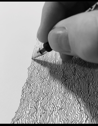 A drawing featuring lines being drawn in pen in the right two thirds of the image. In the top right corner are two fingers holding a pen.