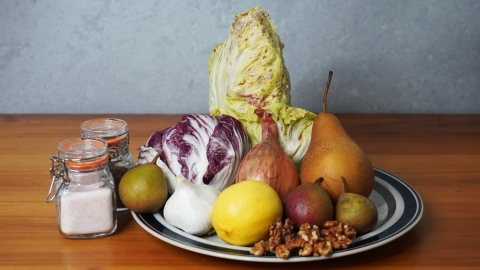 A photo of the ingrediants for the salad. Two different kinds of radicchio, garlic, pears, lemon, garlic and walnuts are arranged on a plate beside jars of salt and pepper.