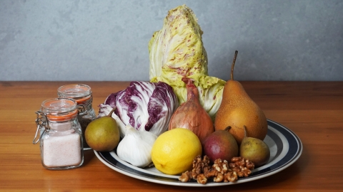A photo of the ingrediants for the salad. Two different kinds of radicchio, garlic, pears, lemon, garlic and walnuts are arranged on a plate beside jars of salt and pepper.