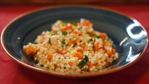 A blue plate on a red tableclothe. In it is a lump of couscous and sweet potato salad! 