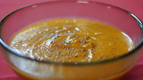 Shot of a clear bowl with an orange soup topped with ground black pepper.