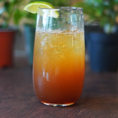 A dark and stormy in a tall clear glass, with a lime wedge on the rim. 