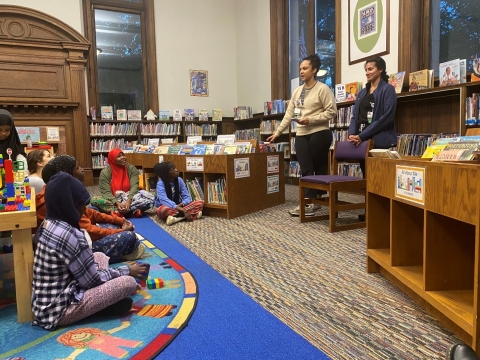 Two people in a library speaking to families seated on the floor.