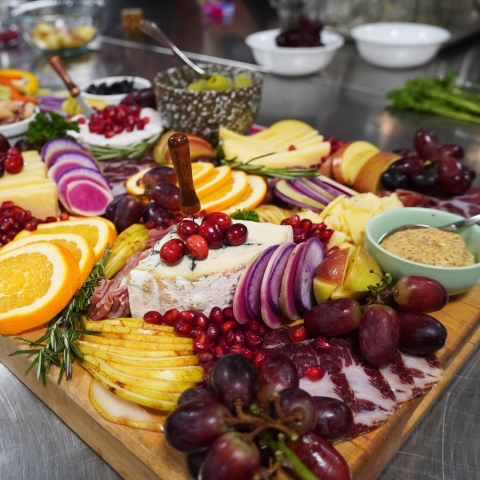 a board full of cheese, veggies, fruits, and spreads