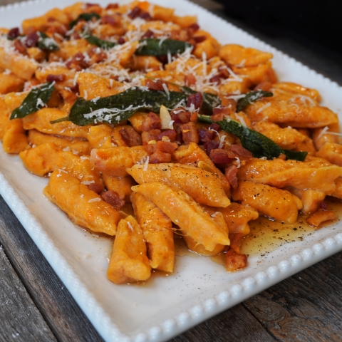 A corner shot of the gnocchi plated on a square white plate. Its topped with fried sage, and parmesean cheese!