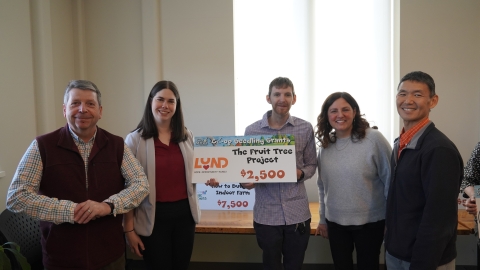 Five people gathered around a sign that says "Lund - The Fruit Tree Project - $2,500"