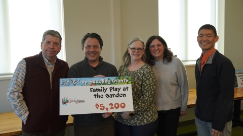 A group of people gathered around a sign that says "Family Play at the Garden - $5,200"