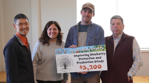 A group of people gathered around a sign that says "Improving Blueberry Protection and Production Study - $3,200"