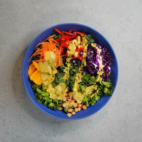 A straight down shot of the bowl of salad. On it you can see the peppers, carrots, cabbage, chickpeas, cilantro, and peas. Dressing is drizzled over all of it. 