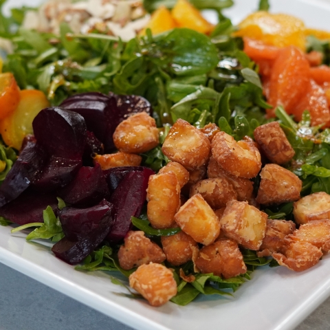 a close up shot of the salad. in the front are the blocks of fried halloumi, beside them are the sliced red beats. Behind them and out of focus are the rest of the salad's toppings.