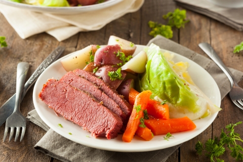 Corned beef, cabbage, potatos, and carrots sit on a white plate on a rustic looking table!