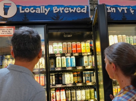 a man and woman look at a selection of beer in the cooler