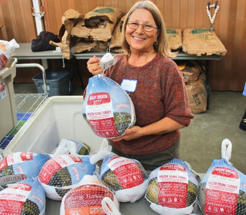 a woman holds up a donated turkey among other donated turkeys