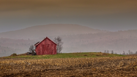 A photo of a red barn with a field in the forefront and a mountain range in the background